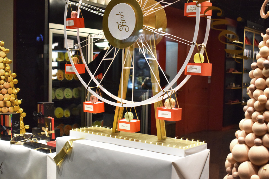 Scénographie vitrine de Noël pour un chocolatier : grande roue aniée, cadeaux et sapins en chocolat