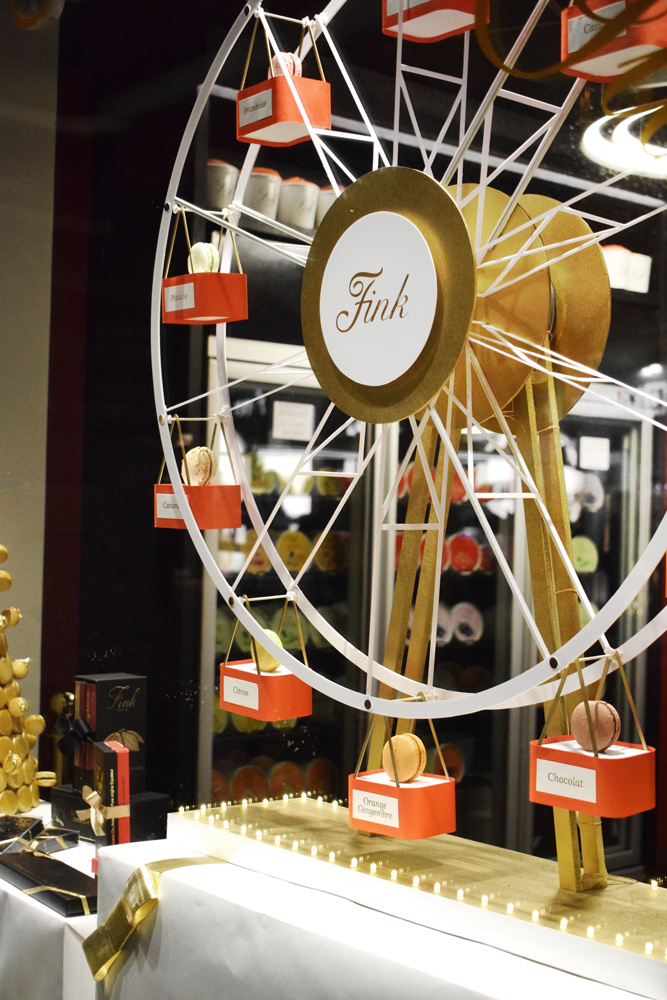 Grande roue animée et illuminée avec de petites nacelles à macarons dans la vitrine d'un chocolatier