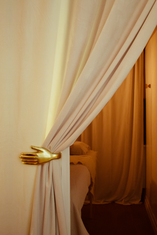 Une main en laiton massive ouvre un rideau de velours blanc qui invite à rentrer dans la cabine de massage chez Spatiu